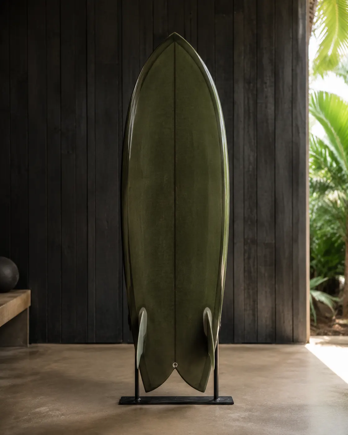 An olive-green twin-fin fish with a swallow tail, standing on a rack against dark timber.