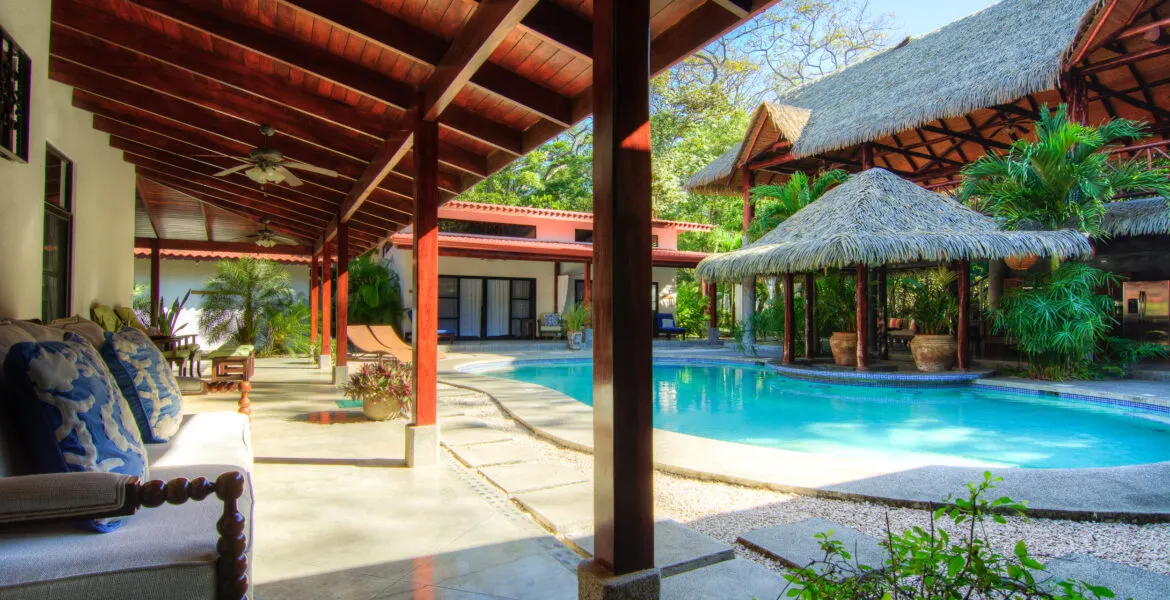 The pool wrapping around the thatched palapa bar, with the submerged blue-tile bar stools visible at right and the tall thatched main lodge behind.