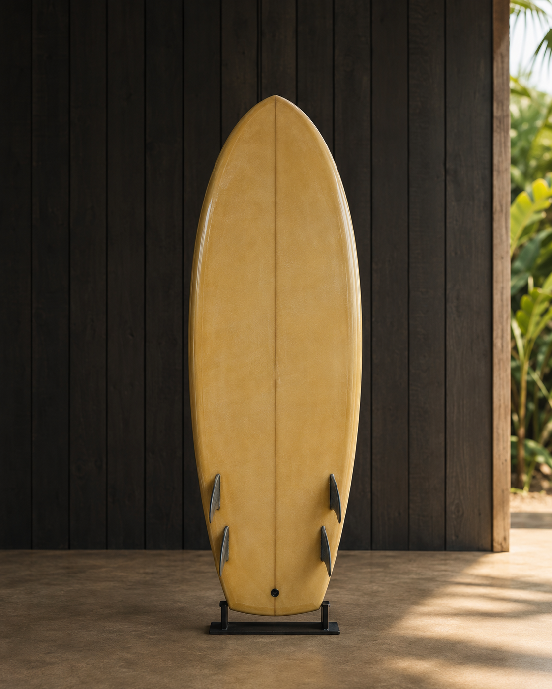 A mustard-tinted groveler with a wide round nose and quad fins, standing on a rack against dark timber.
