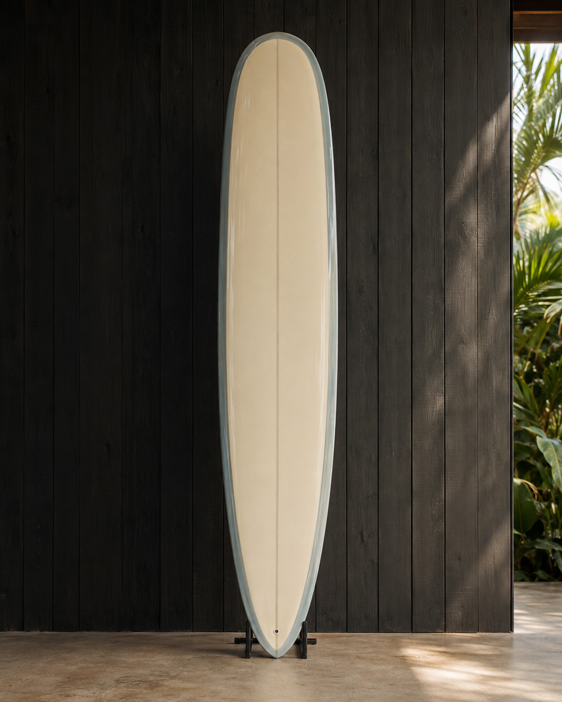 A cream longboard with pale blue rails and a single fin, standing on a rack against dark timber.